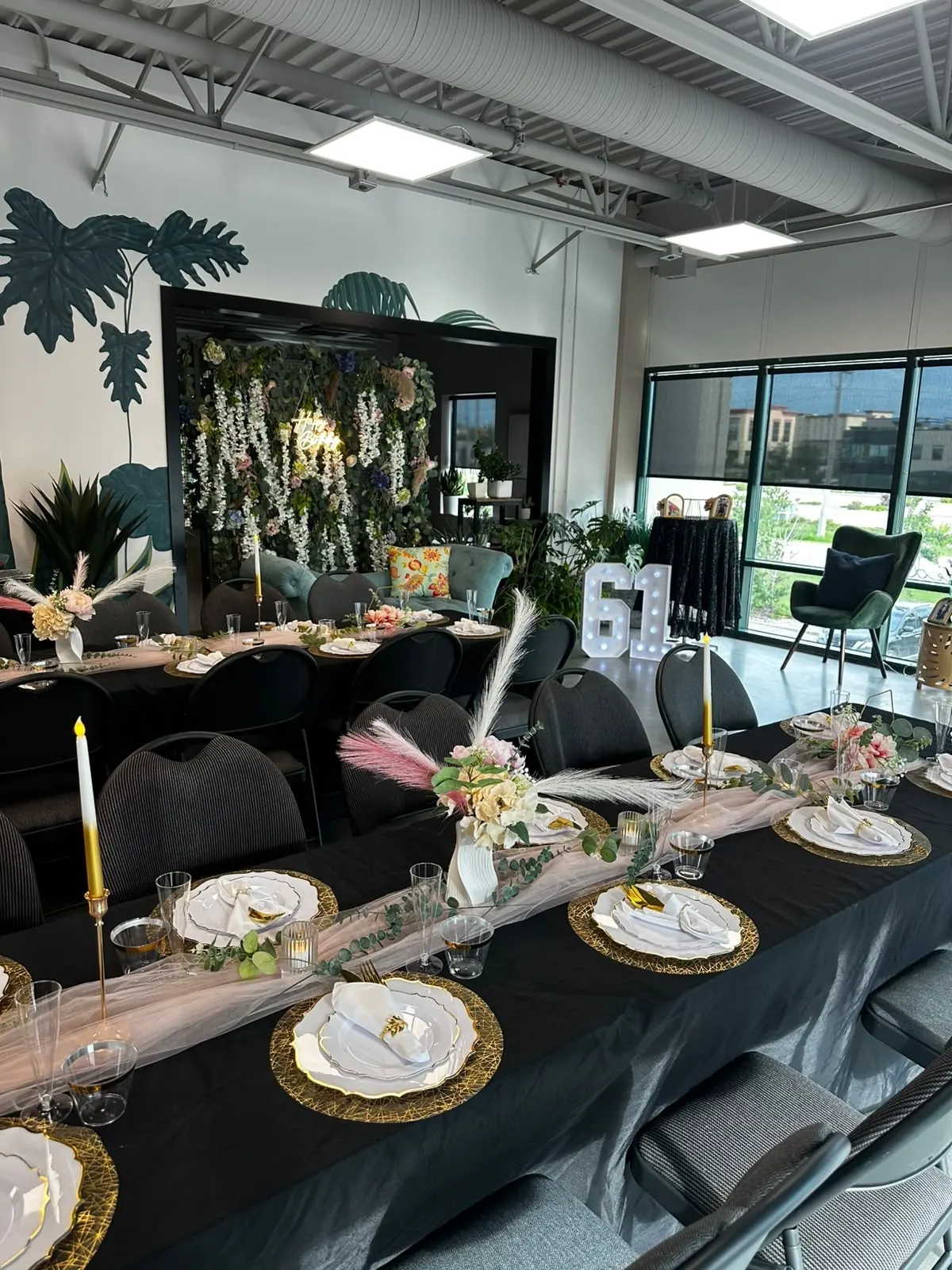 A long black-linen birthday table with gold chargers and floral centrepieces in a bright hall