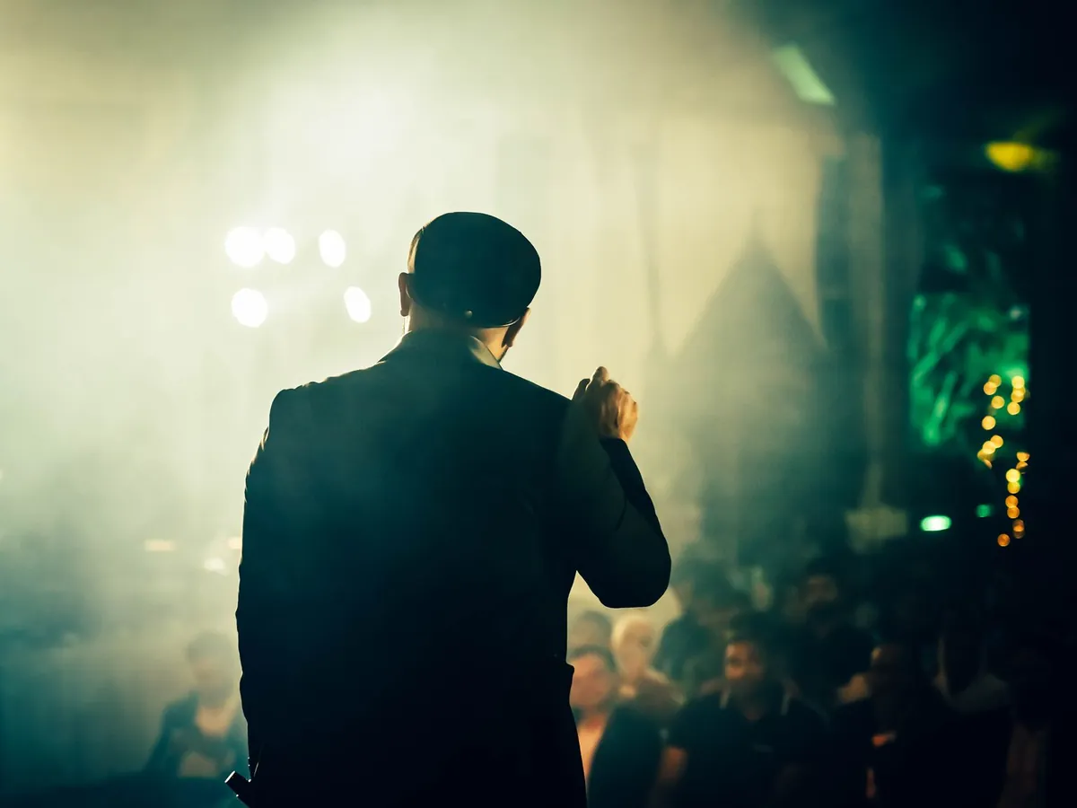 An MC seen from behind, hosting a crowd at an evening event